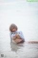 A woman in a white shirt is sitting in the water.