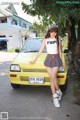 A woman standing next to a yellow car on a street.