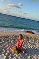 A woman sitting on the beach with two coconuts.