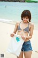 A woman in a bikini top and denim shorts on the beach.