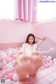 A woman laying in a pink bathtub filled with pink and white balloons.